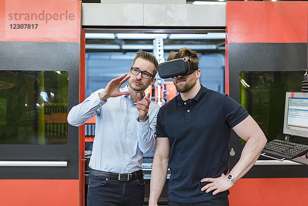 Mann erklärt Maschine dem Kollegen mit VR-Brille in der Fabrik