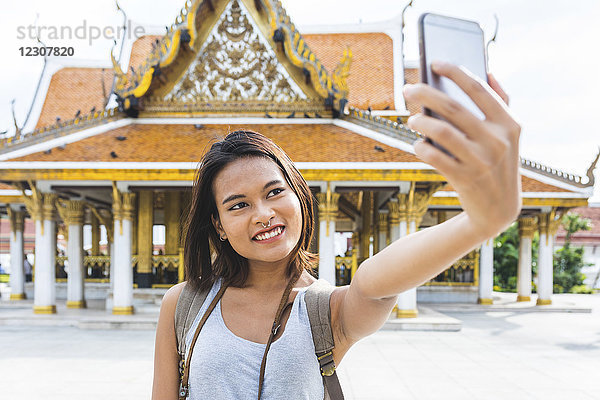 Thailand  Bangkok  Porträt eines lächelnden Touristen  der sich selbst mit dem Smartphone fotografiert.