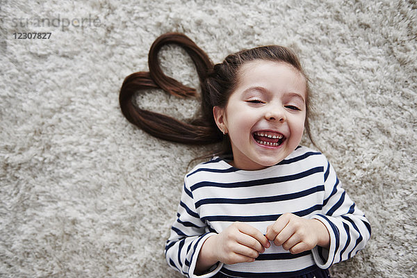 Porträt eines lachenden kleinen Mädchens  das auf einem Teppich liegt.