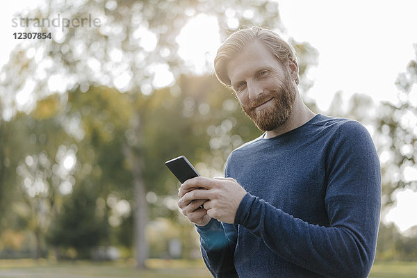 Porträt eines lächelnden Mannes mit Handy im Park