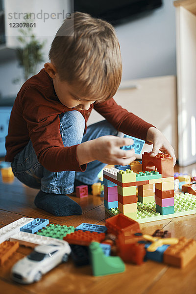 Kleiner Junge  der zu Hause mit Bausteinen auf dem Boden spielt.
