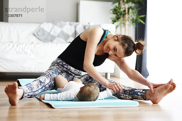 Mutter mit Baby beim Training auf der Yogamatte zu Hause
