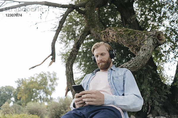 Mann mit Smartphone und Kopfhörer beim Musikhören im Freien