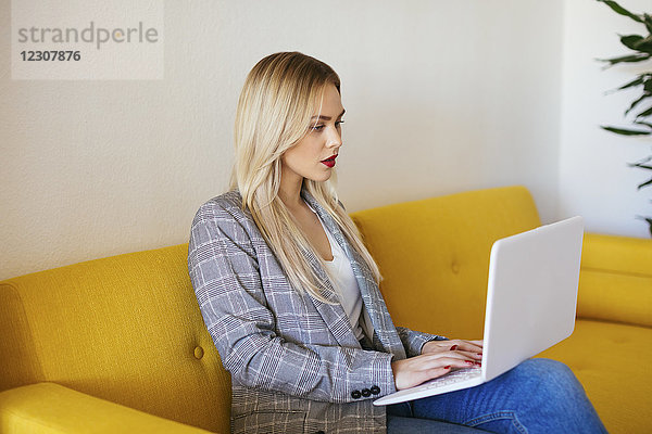 Geschäftsfrau auf gelber Couch sitzend  mit Laptop