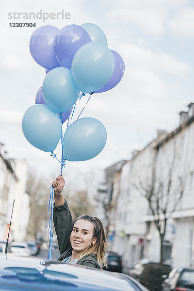 Porträt einer lächelnden Frau mit blauen Luftballons auf der Straße