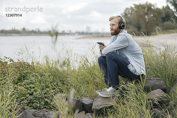 Deutschland  Düsseldorf  Mann hört Musik mit Kopfhörer und Smartphone in der Natur
