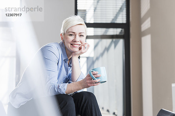 Porträt einer lächelnden Frau  die im Büro auf dem Tisch sitzt.