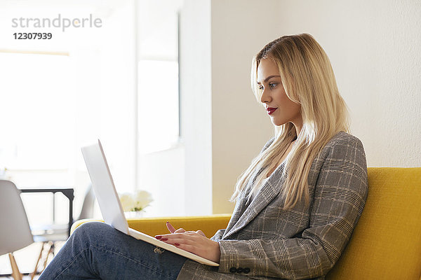 Geschäftsfrau auf gelber Couch sitzend  mit Laptop