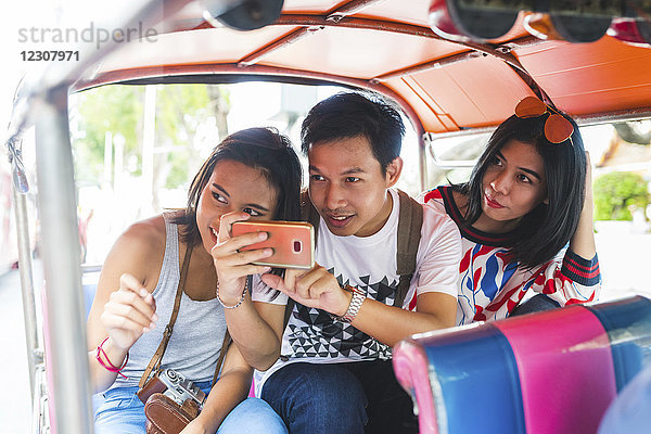 Thailand  Bangkok  drei Freunde auf Tuk Tuk Tuk beim Fotografieren mit dem Smartphone