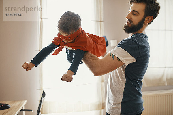 Vater spielt mit seinem kleinen Sohn  verkleidet als Superheld.