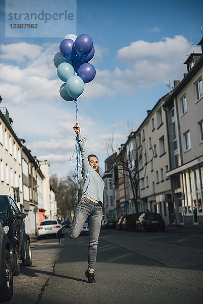 Lächelnde Frau mit blauen Luftballons auf der Straße