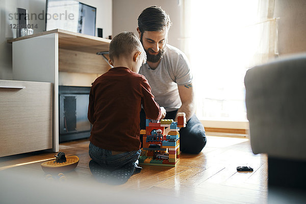 Vater und Sohn sitzen zu Hause auf dem Boden und spielen mit Bausteinen.