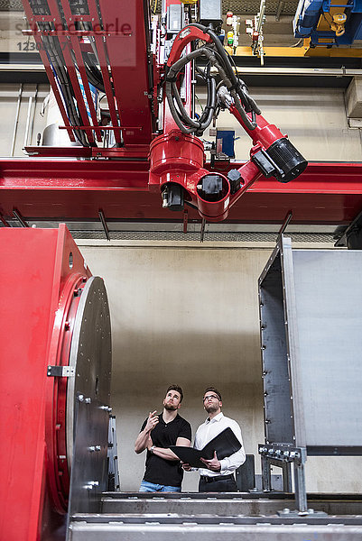 Zwei Männer mit Falzapparat schauen auf die Maschine in der Fabrikhalle