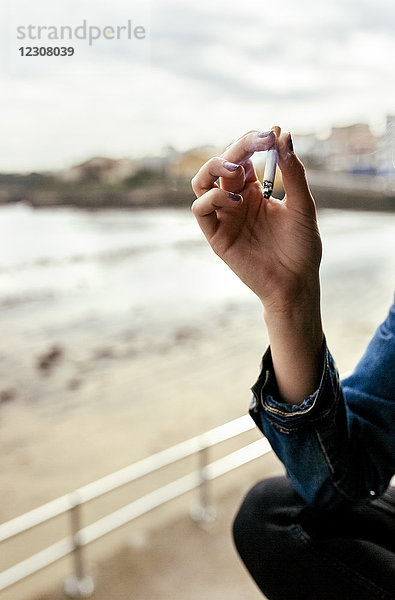 Hand einer Frau  die in einem Küstendorf eine Zigarette raucht.