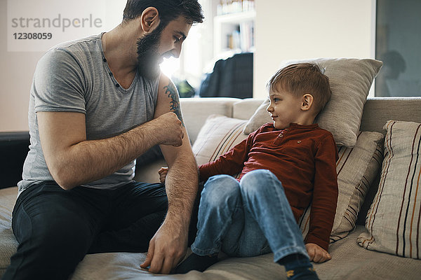 Vater sitzt auf der Couch mit kleinem Sohn  der sein Tattoo zeigt.