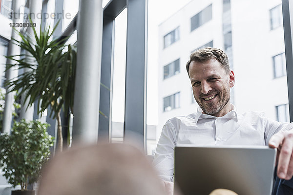 Portrait eines lächelnden Geschäftsmannes mit Laptop in der Bürolounge