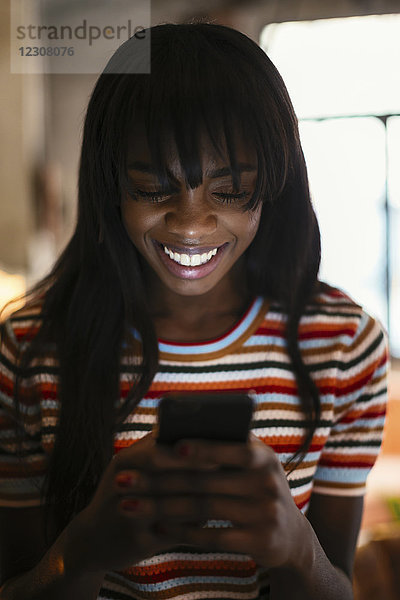 Porträt einer glücklichen jungen Frau beim Blick aufs Handy