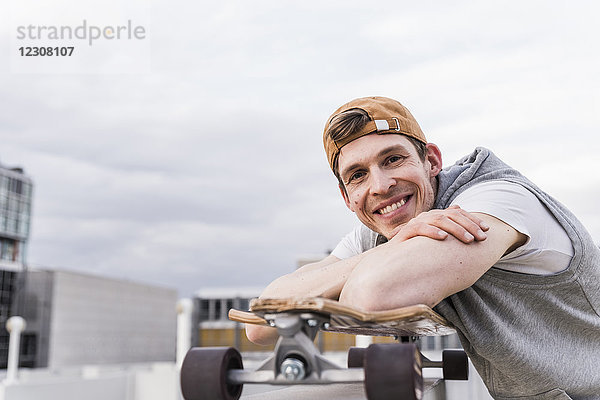 Porträt eines lächelnden Mannes mit Skateboard an einer Wand lehnend
