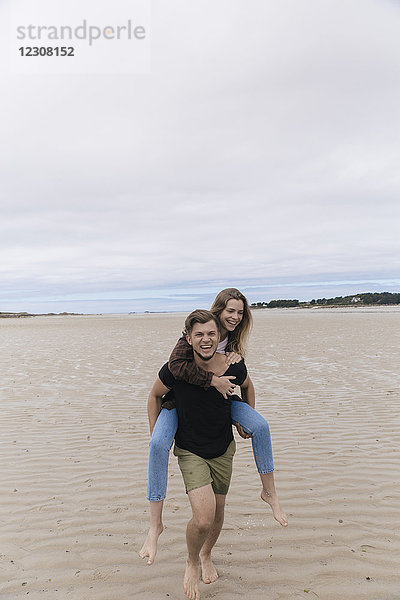 Frankreich  Bretagne  Guisseny  glücklicher junger Mann mit Freundin Huckepack am Strand
