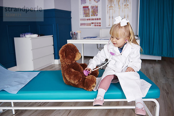 Mädchen mit Stethoskop untersucht Teddy in der Arztpraxis