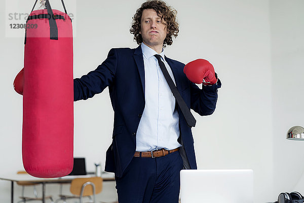 Gestresster Geschäftsmann schlägt Boxsack mit Boxhandschuhen ins Büro