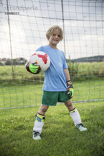 Porträt eines lächelnden jungen Fußballtorhüters  der den Ball auf dem Fußballplatz hält.