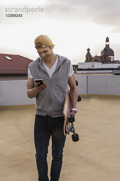 Lächelnder Mann mit Handy und Skateboard im Parkhaus