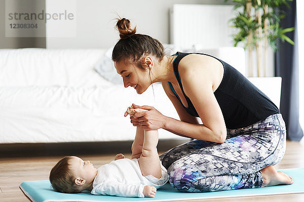 Mutter mit Baby beim Training auf der Yogamatte zu Hause
