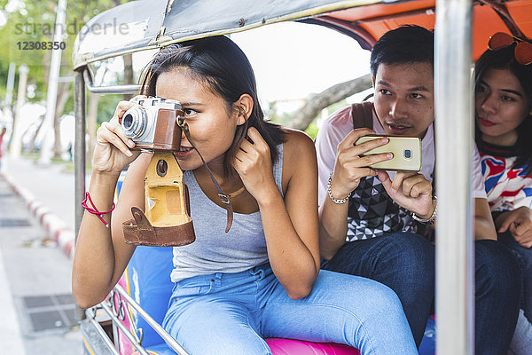 Thailand  Bangkok  drei Freunde auf Tuk Tuk Tuk beim Fotografieren mit dem Smartphone