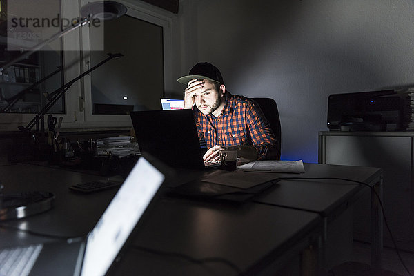Porträt eines Freiberuflers  der nachts am Schreibtisch sitzt und am Laptop arbeitet.