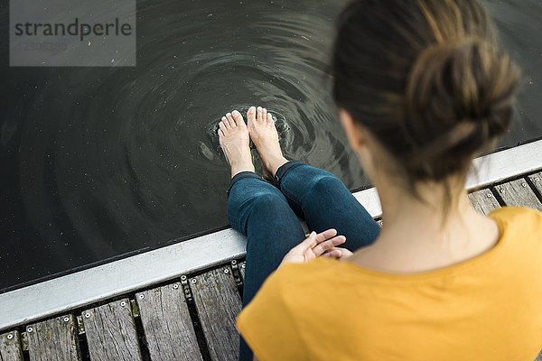 Frau sitzt auf einem Steg an einem See mit Füßen im Wasser