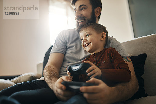 Glücklicher Vater und kleiner Sohn sitzen zusammen auf der Couch und spielen Computerspiel.