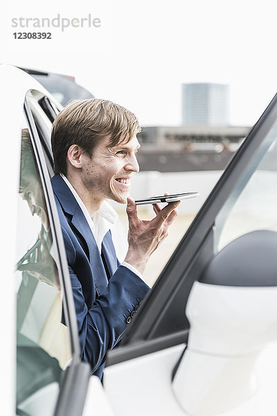 Lächelnder Geschäftsmann mit Smartphone im Auto