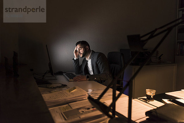 Nachdenklicher junger Geschäftsmann sitzt nachts am Schreibtisch im Büro.
