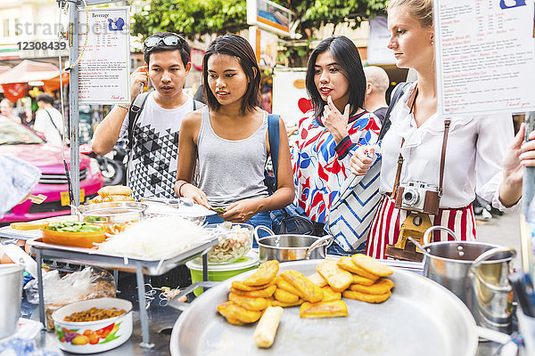 Thailand  Bangkok  Khao San Road  Gruppe von Freunden  die auf dem Straßenmarkt lokale Speisen wählen