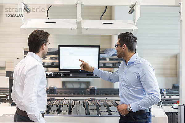 Zwei Geschäftsleute im Gespräch am Bildschirm in der modernen Fabrik