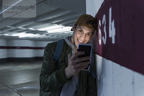 Lächelnder Mann schaut auf leuchtendes Smartphone im Parkhaus
