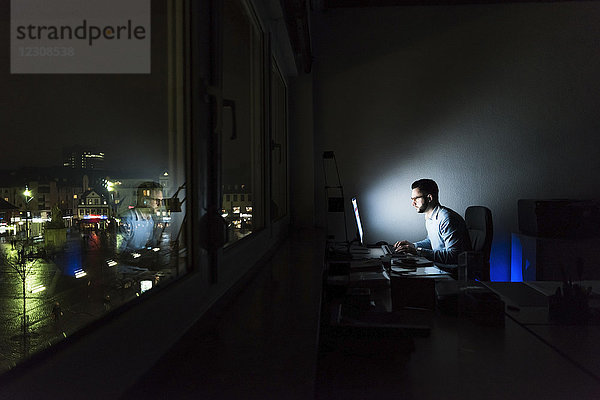 Geschäftsmann bei der Arbeit am Computer im dunklen Büro