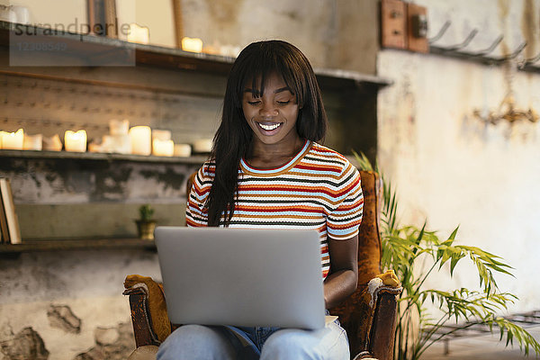 Porträt einer lächelnden jungen Frau auf einem Ledersessel mit Laptop