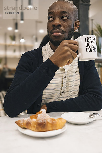 Mann mit Croissant und Tasse Kaffee in einem Cafe  der sich umsieht