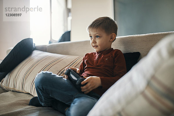 Portrait eines kleinen Jungen  der auf der Couch sitzt und Computerspiel spielt.