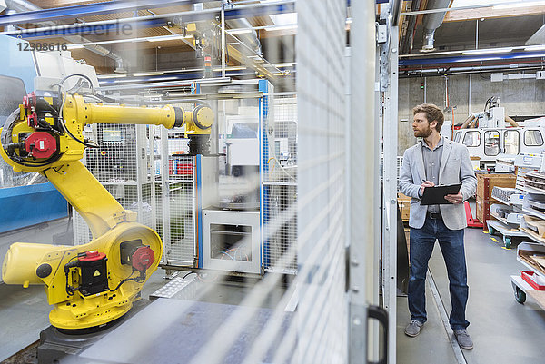 Geschäftsmann betrachtet Industrieroboter in einer modernen Fabrik