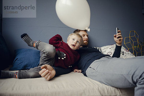 Vater liest SMS  während der Sohn mit einem Ballon spielt.