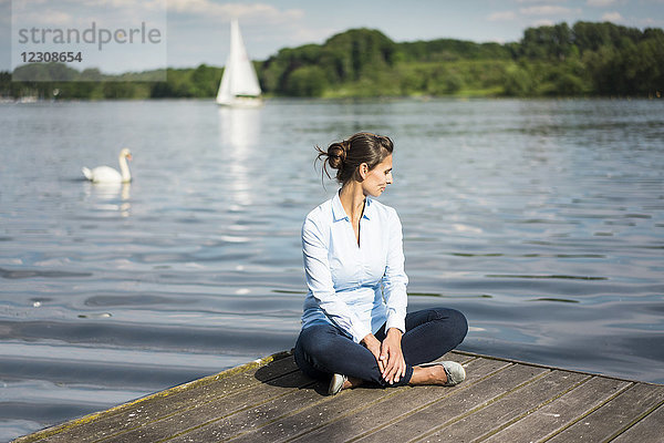 Entspannte Frau sitzt auf einem Steg am See