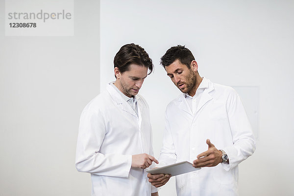 Zwei Männer in Arbeitsmänteln teilen sich die Tablette.