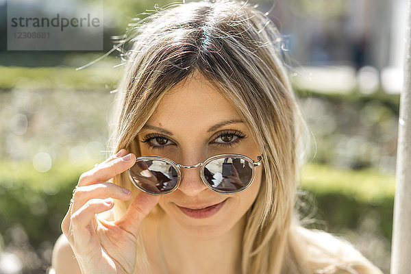 Porträt einer lächelnden jungen Frau mit verspiegelter Sonnenbrille