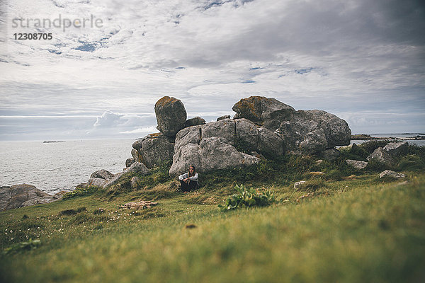 Frankreich  Bretagne  Landeda  Dunes de Sainte-Marguerite  junge Frau an den Felsen an der Küste sitzend