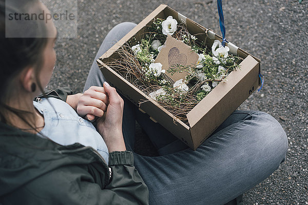 Frau mit Blumenarrangement im Karton auf dem Boden sitzend
