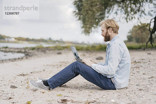 Deutschland  Düsseldorf  Mann am Strand sitzend mit Laptop