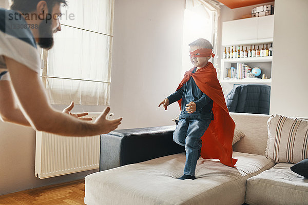 Vater spielt mit seinem kleinen Sohn  verkleidet als Superheld zu Hause.
